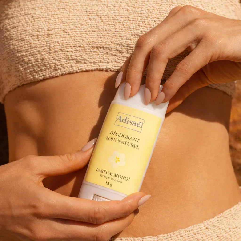 Déodorant soin naturel parfum monoï tenu par une femme, exposé au soleil sur la peau