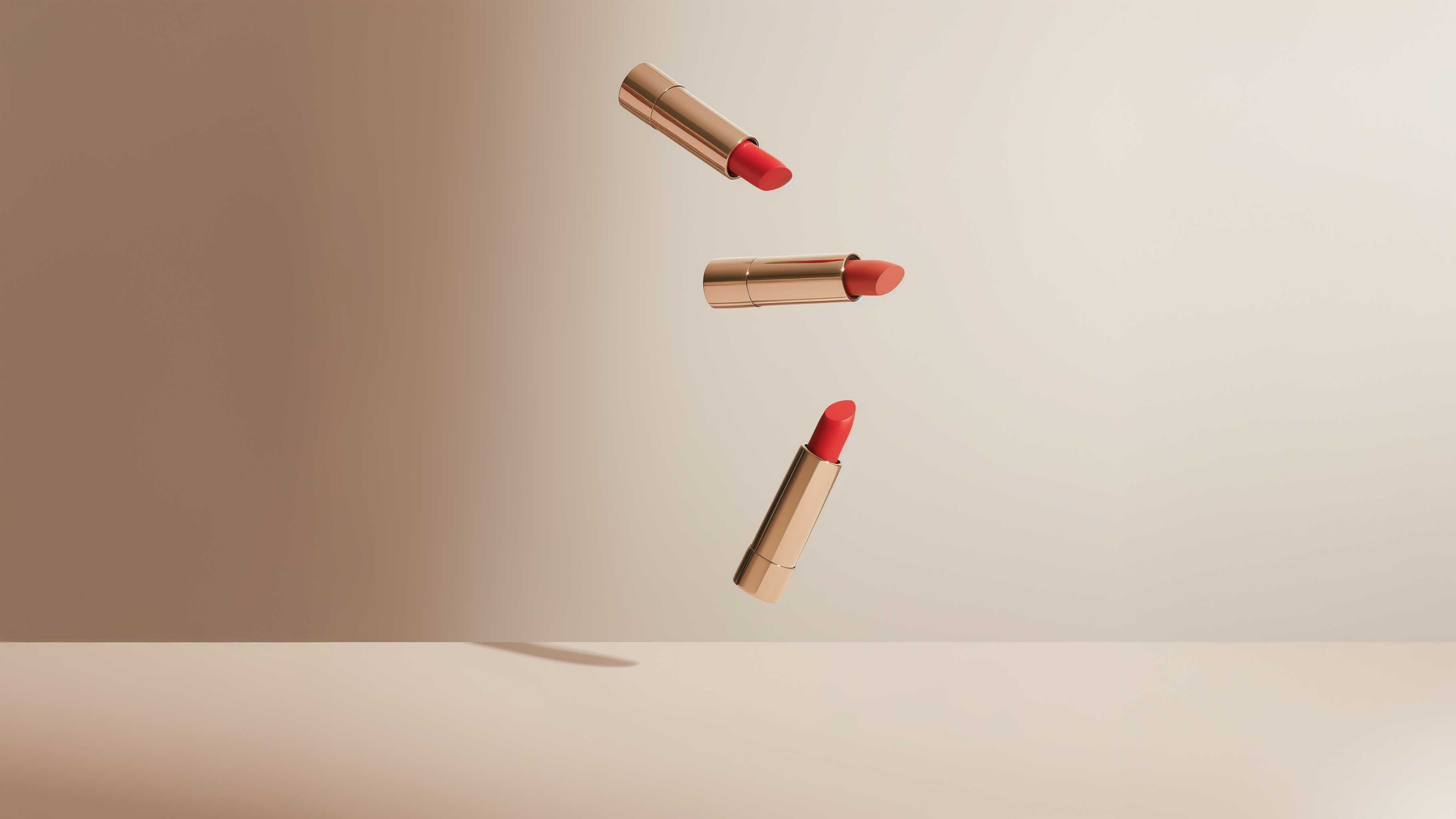 Trois rouges à lèvres rouges flottant sur fond beige, maquillage beauté moderne.