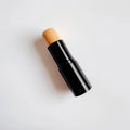 Stick de fond de teint beige sur fond blanc, produit maquillage visage élégant