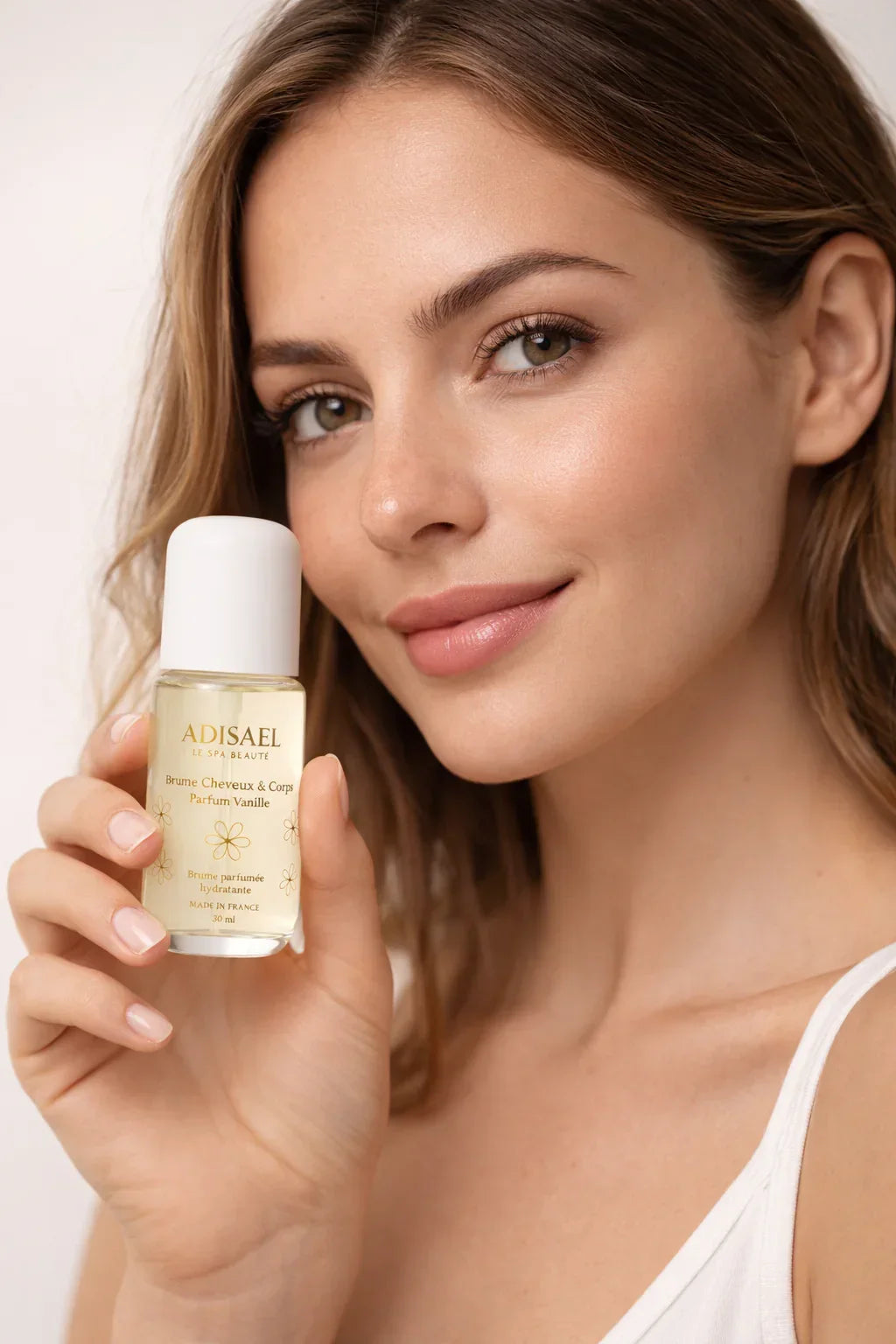 Femme souriante tenant une brume cheveux et corps parfum vanille, flacon 30ml.